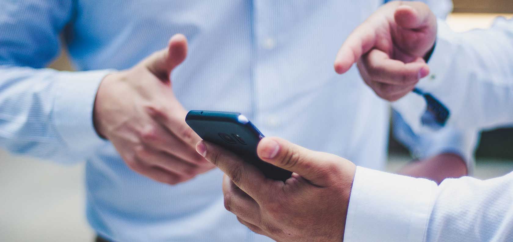 Ein Mann in einem weißen Hemd blickt auf ein Smartphone in seinen Händen.